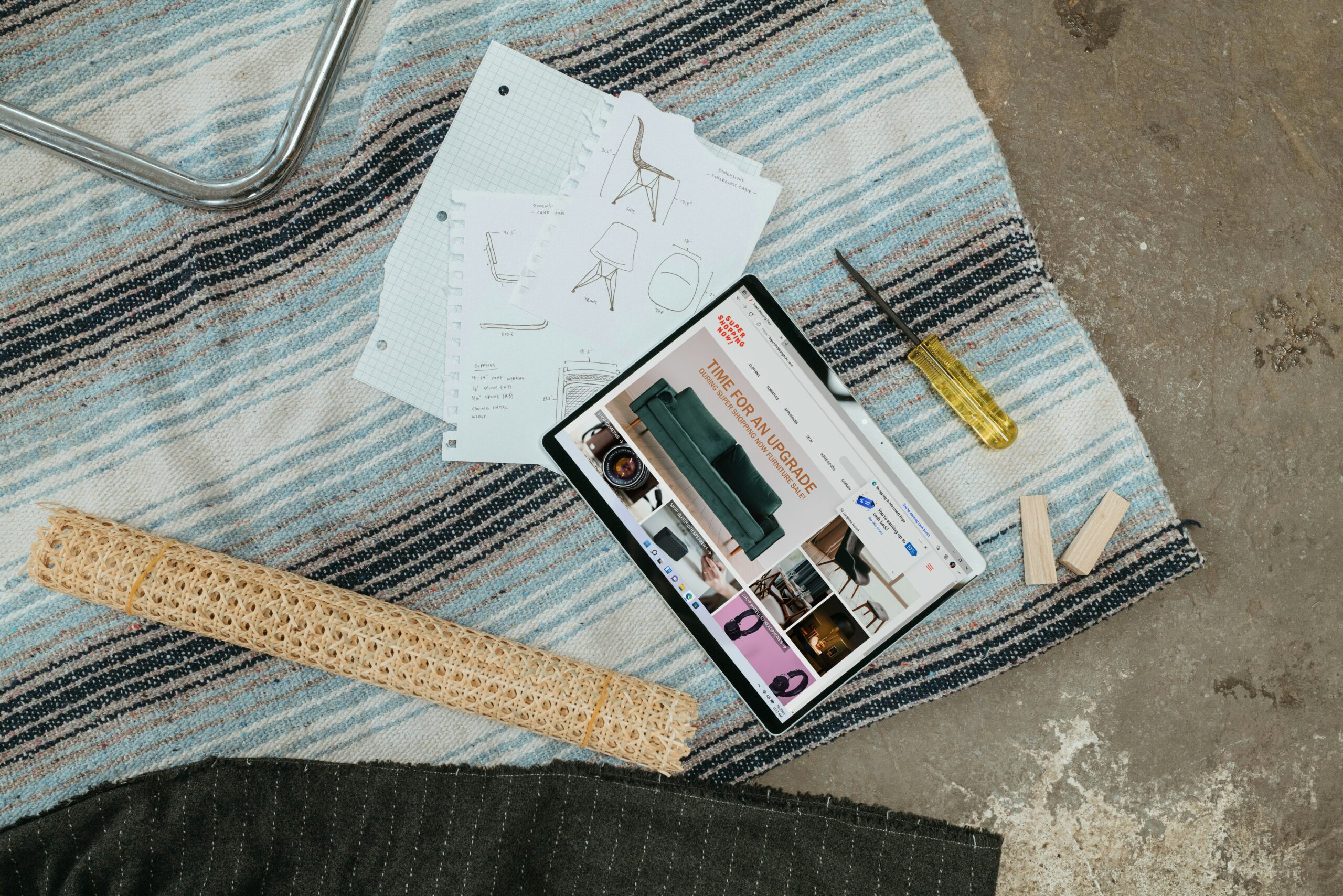 Stock image of an ipad with furniture options and sketches on the side laying on a blanket placed over a concrete floor